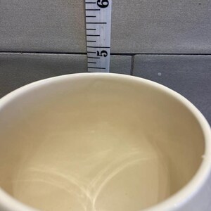 May include: A white ceramic mug with a smooth, glossy finish. The inside of the mug is empty.