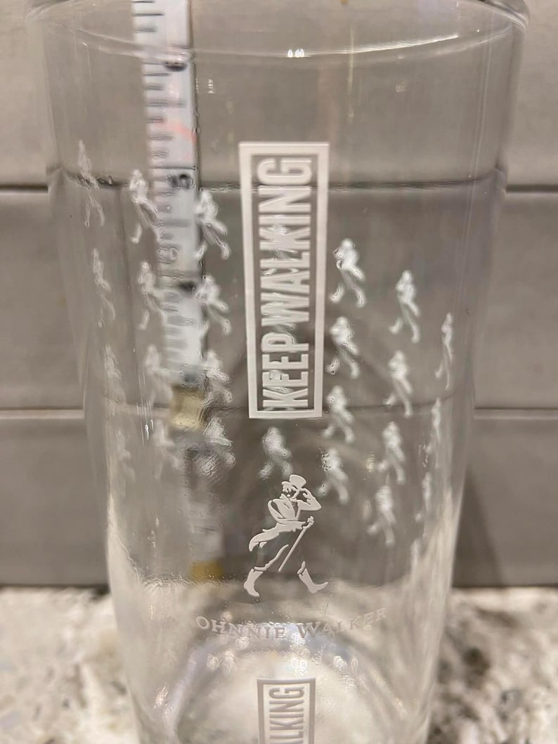 May include: Clear pint glass with the text "KEEP WALKING" in a white rectangular box. The glass features a white silhouette of a man walking with a cane, and small white figures walking around the glass. The words "JOHNNIE WALKER" are printed at the bottom.
