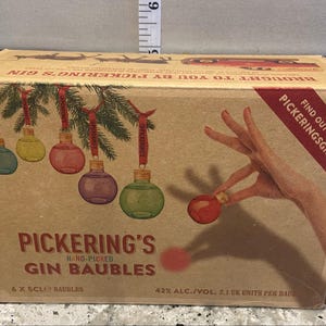 May include: A box of six small glass ornaments filled with gin. The ornaments are red, green, blue, and clear. The box is brown with a red and white label that says "Pickering's Gin Baubles".