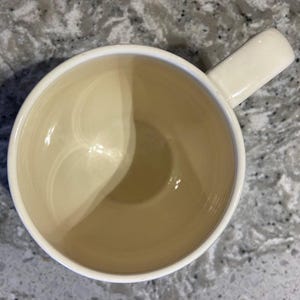 May include: A white ceramic mug with a smooth, glossy finish. The mug has a rounded shape and a handle on the right side.