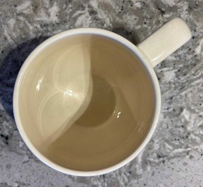May include: A white ceramic mug with a smooth, glossy finish. The mug has a rounded shape and a handle on the right side.