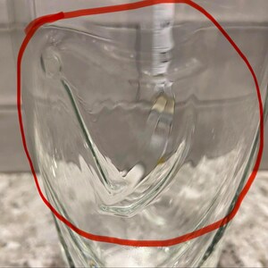 May include: A clear glass with a unique, curved design. The glass has a smooth, transparent surface, with a distinctive shape that adds visual interest. The glass is likely used for beverages.