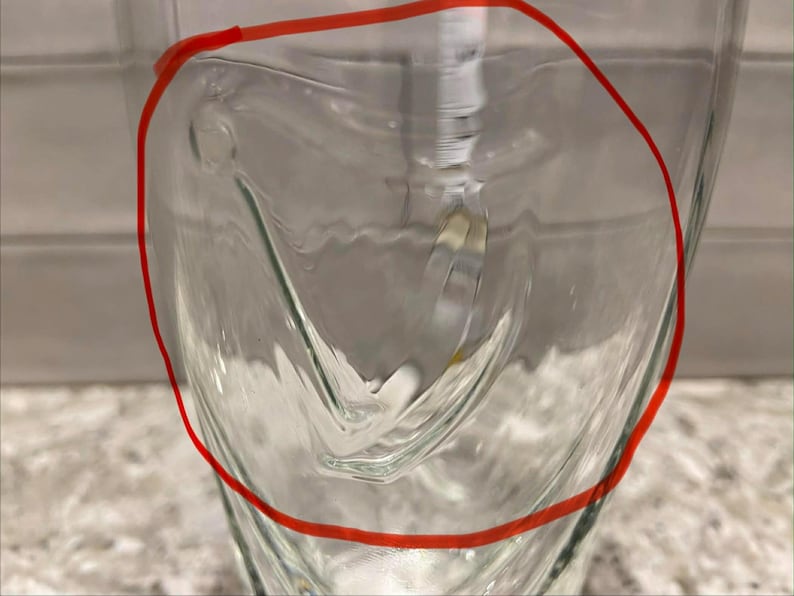 May include: A clear glass with a unique, curved design. The glass has a smooth, transparent surface, with a distinctive shape that adds visual interest. The glass is likely used for beverages.