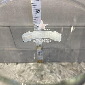 以下が含まれることがあります： ハイネケンのロゴと白い星が入った透明なガラスのビールグラス。グラス内にはメジャーが置かれ、約15cmの測定値を示しています。