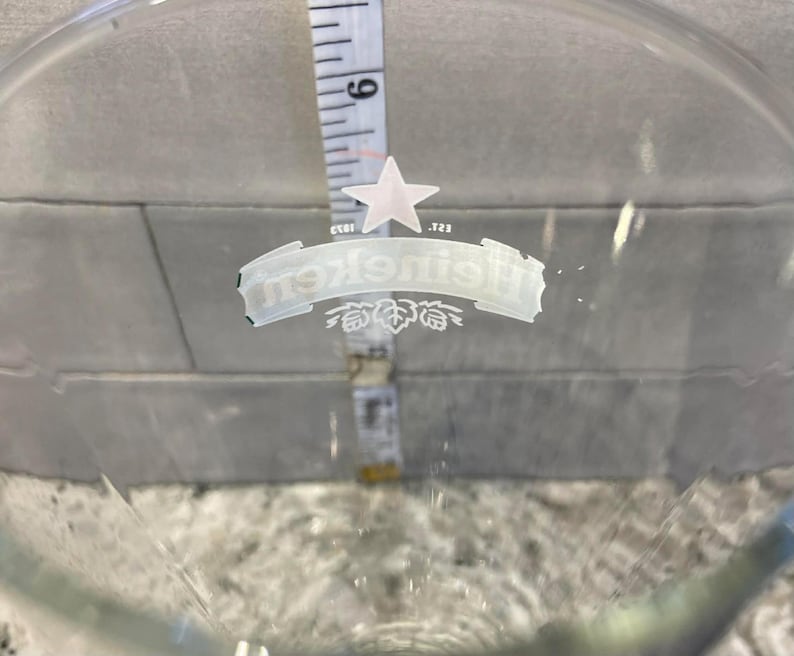 以下が含まれることがあります： ハイネケンのロゴと白い星が入った透明なガラスのビールグラス。グラス内にはメジャーが置かれ、約15cmの測定値を示しています。