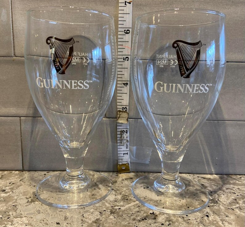 May include: Two clear Guinness beer glasses, each with the Guinness logo. The glasses are about 15 cm tall. They have a stemmed base and a tulip-shaped bowl, designed for enjoying stout.