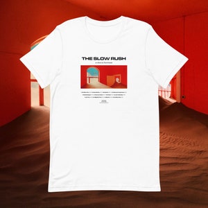 May include: White t-shirt with a graphic of the album cover for "The Slow Rush" by Tame Impala. The album cover features a red room with two doorways and a sandy floor.