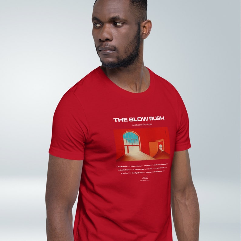 May include: Red t-shirt with a white graphic of the album cover for "The Slow Rush" by Tame Impala. The album cover features a red and orange background with a window and a doorway.