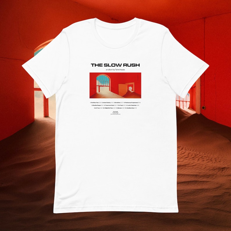 May include: White t-shirt with a graphic of the album cover for "The Slow Rush" by Tame Impala. The album cover features a red room with two doorways and a sandy floor.