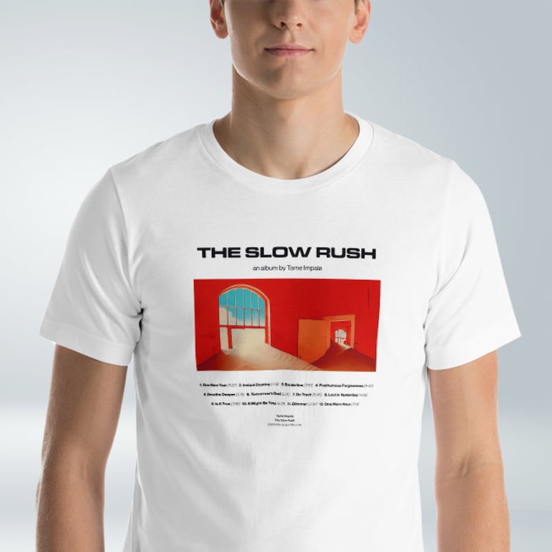 May include: White t-shirt with a black and white image of the album cover for "The Slow Rush" by Tame Impala. The album cover features a red room with a window and a doorway. The album title and artist name are printed in black text.