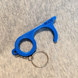 May include: A blue plastic keychain tool with a loop on one end and a hook on the other. The keychain has a silver metal ring and chain. The tool is labeled "M42C".