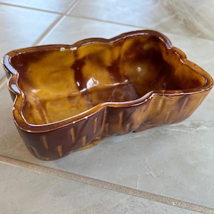 May include: A brown and yellow ceramic planter with a textured, wood-like design. The planter is empty and ready for a plant.