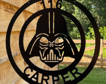 May include: A circular black metal sign hanging from a black bracket by two chains. The sign features a cutout of a helmeted character face in the center, with the number 116 at the top and the name CARPER in capital letters at the bottom.