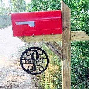 May include: A red mailbox with a black metal sign that says "EST. 2017 PRINCE" hanging from it. The mailbox is mounted on a wooden post.