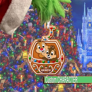 May include: A gingerbread-style Christmas ornament shaped like a gondola, featuring two cartoon chipmunks inside. The ornament is decorated with colorful icing dots and includes a rectangular plaque with the name KRISTIE printed in white letters.