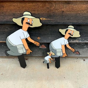 Puede incluir: Tres estacas de jard&iacute;n con un personaje de dibujos animados con bigote, que lleva un sombrero beige de ala ancha, una camiseta blanca y pantalones grises. Cada figura est&aacute; en cuclillas, sosteniendo una peque&ntilde;a paleta con tierra marr&oacute;n.