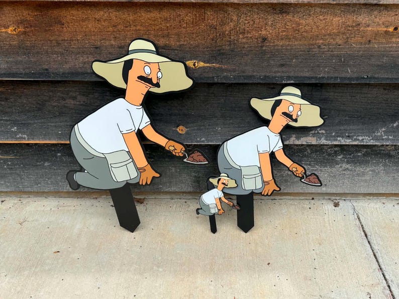 Puede incluir: Tres estacas de jard&iacute;n con un personaje de dibujos animados con bigote, que lleva un sombrero beige de ala ancha, una camiseta blanca y pantalones grises. Cada figura est&aacute; en cuclillas, sosteniendo una peque&ntilde;a paleta con tierra marr&oacute;n.