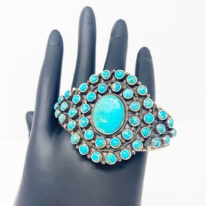 Könnte beinhalten: Ein silbernes Armband mit einem großen Türkis-Stein, der von kleineren Türkis-Steinen umgeben ist.