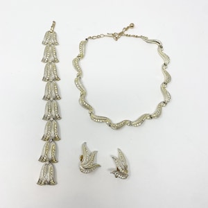Könnte beinhalten: Ein silberfarbener Schmuck-Set mit einer Halskette, einem Armband und Ohrringen. Die Halskette und das Armband haben ein wellenförmiges Design mit kleinen, klaren Steinen. Die Ohrringe sind blattförmig mit klaren Steinen.