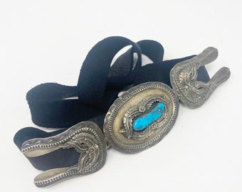 May include: A black suede belt with two silver and turquoise buckles. The belt is decorated with intricate floral designs.
