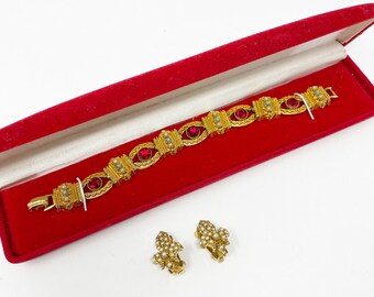 Puede incluir: Un brazalete de oro con piedras rojas y azules en una caja de terciopelo rojo. También se incluye un par de pendientes de oro con detalles de perlas.