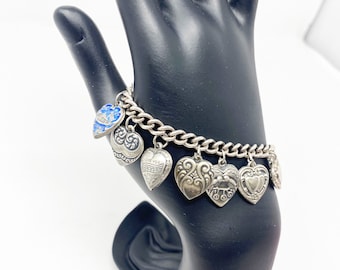 May include: A silver charm bracelet with a chain and multiple heart-shaped charms. The charms have different designs, including a blue enamel heart, a heart with the words "I Love You" and a heart with a floral design.