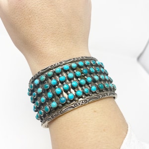 Puede incluir: Un brazalete de plata con una fila de piedras turquesa. El brazalete está decorado con un diseño de plata.