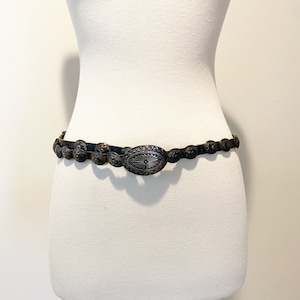 May include: A black leather belt with a silver oval buckle and decorative silver accents. The buckle has a floral design.