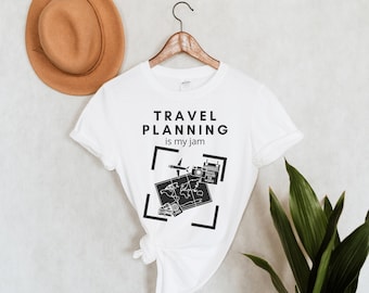 May include: White t-shirt with a black graphic design that says "TRAVEL PLANNING is my jam". The graphic includes a world map, a plane, a camera, and a passport.