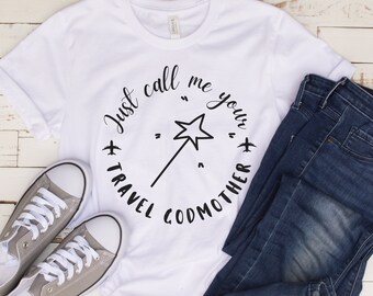 May include: White t-shirt with a black graphic that says "Just call me your travel godmother" with a star and a wand in the middle.