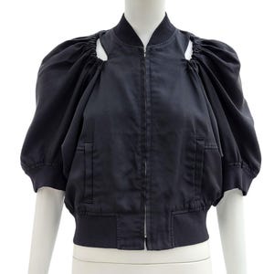 Peut inclure: Veste de bombardier bleu marine foncé avec des manches courtes bouffantes et une fermeture éclair sur le devant. La veste a un ourlet et des poignets côtelés, et des détails découpés sur les épaules. La veste est présentée sur un mannequin.