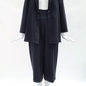May include: A dark navy blue two-piece set consisting of a long-sleeved blazer with a notched lapel and two small silver-toned buttons, paired with matching high-waisted cropped trousers that feature a wide-leg silhouette and a clean, simple finish.