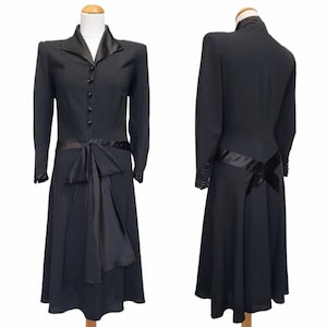 Puede incluir: Un vestido negro con un lazo de sat&eacute;n en la cintura y mangas largas. El vestido tiene un corpi&ntilde;o ajustado y una falda acampanada.