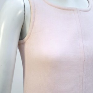 Puede incluir: Un vestido rosa p&aacute;lido sin mangas con cuello redondo y una costura vertical en el centro. El vestido se exhibe en un maniqu&iacute;, destacando su dise&ntilde;o simple y elegante. La tela parece ser un tejido de punto suave.