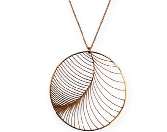 Puede incluir: Un collar con colgante dorado con un gran diseño ovalado calado. El colgante tiene un patrón en forma de hoja con líneas curvas que irradian desde un lado. La cadena es delicada y también dorada, creando un accesorio elegante.