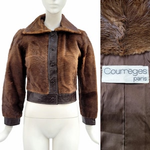 May include: A brown faux fur jacket with a dark brown leather collar, cuffs, and trim. The jacket has a button-up front and the label "Courr&egrave;ges paris" is visible.