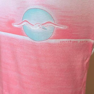 May include: A pink and white ombre t-shirt with a seagull flying over a blue circle. The text "Courr&egrave;ges Paris" is printed on the bottom right corner of the shirt.
