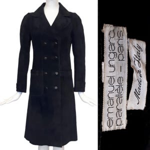 May include: A black suede double-breasted coat with a long silhouette and a patch pocket on the left side. The coat has a label that reads "emanuel ungaro parallele - paris Made in Italy".