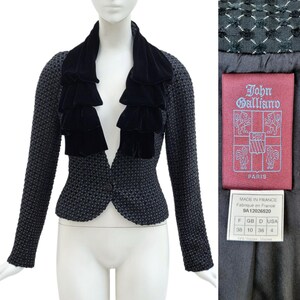 May include: Black and white tweed jacket with a black velvet ruffle collar. The jacket has a single button closure and is labeled "John Galliano, Paris".