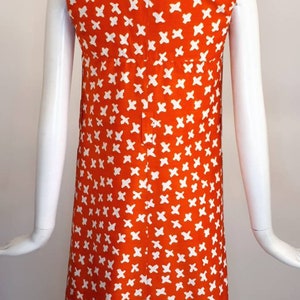 May include: A sleeveless orange dress with a white geometric pattern. The dress has a collared neckline and a button closure down the front.
