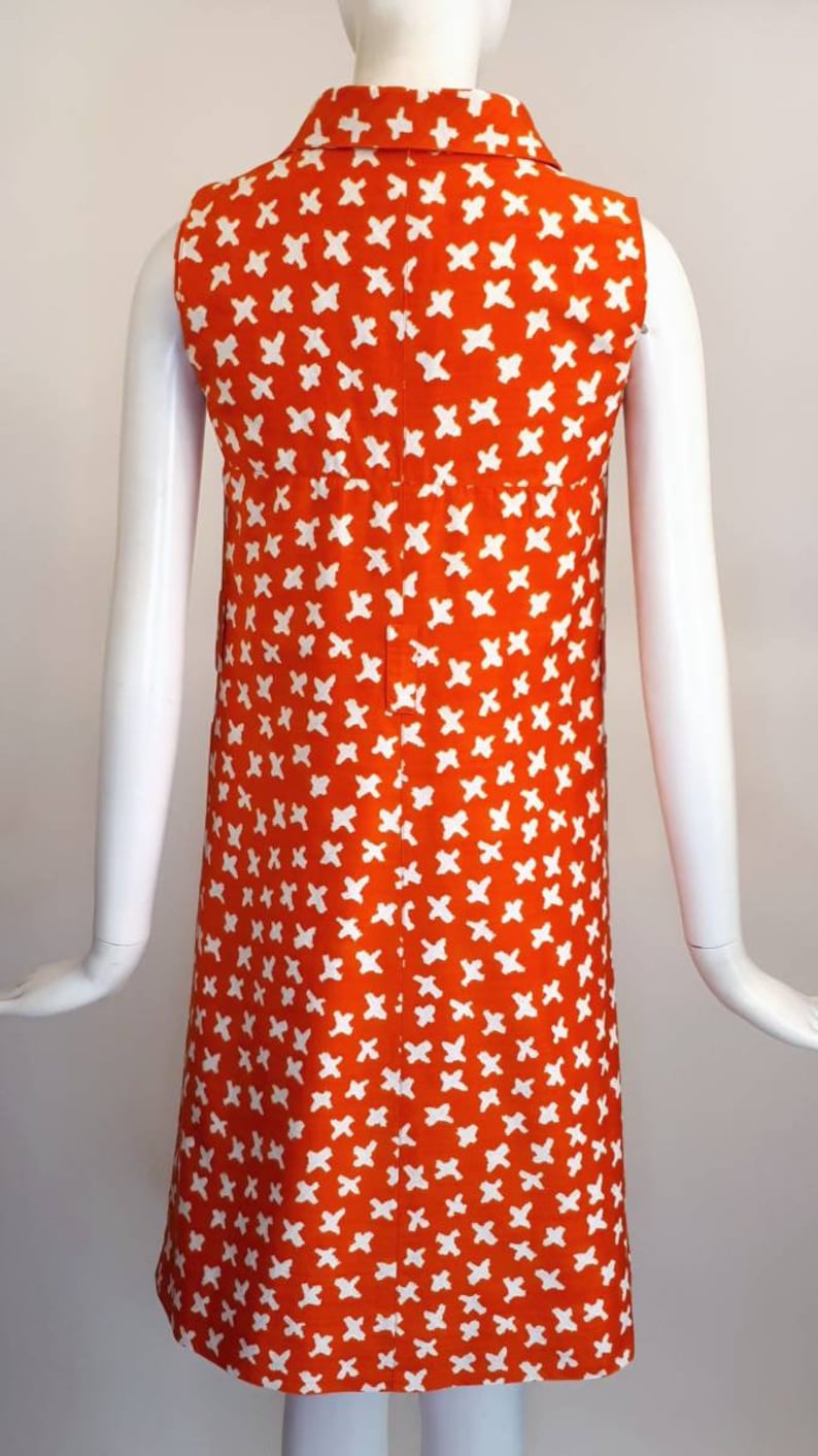 May include: A sleeveless orange dress with a white geometric pattern. The dress has a collared neckline and a button closure down the front.