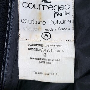 Pu&ograve; includere: Primo piano di un capo nero con un'etichetta bianca con il logo e il testo "courr&egrave;ges paris couture future". L'etichetta include anche "made in france" e istruzioni per la cura. Il tessuto del capo &egrave; visibile.