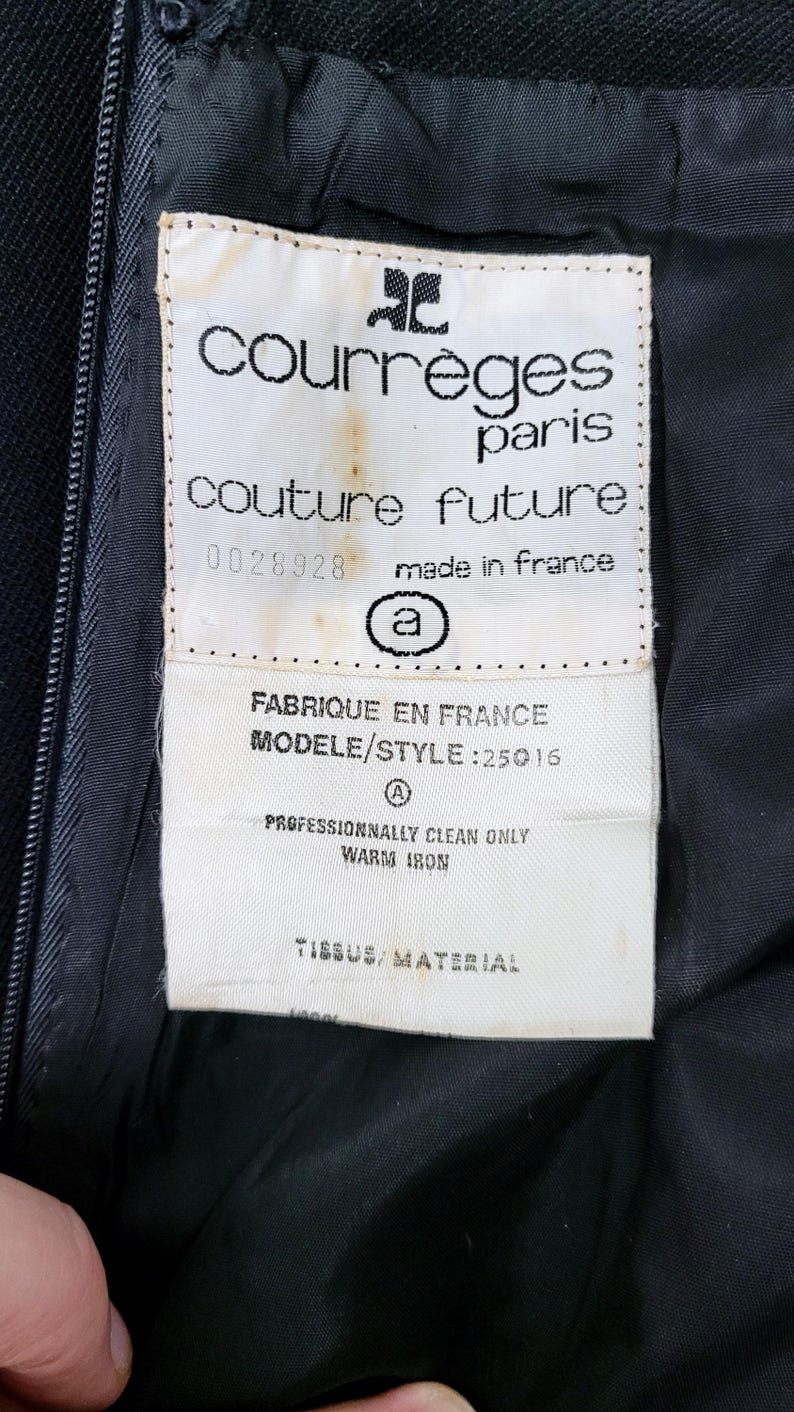 Pu&ograve; includere: Primo piano di un capo nero con un'etichetta bianca con il logo e il testo "courr&egrave;ges paris couture future". L'etichetta include anche "made in france" e istruzioni per la cura. Il tessuto del capo &egrave; visibile.