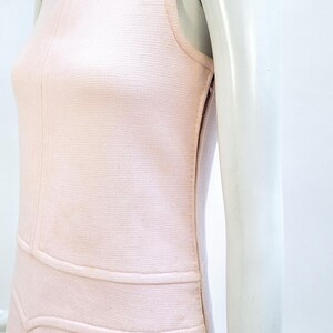 Puede incluir: Vestido rosa claro sin mangas con tejido texturizado. El vestido presenta un cuello redondo, un corpi&ntilde;o entallado y un dise&ntilde;o estructurado con costuras horizontales y verticales. El vestido se exhibe en un maniqu&iacute;.