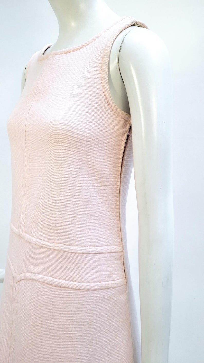 Puede incluir: Vestido rosa claro sin mangas con tejido texturizado. El vestido presenta un cuello redondo, un corpi&ntilde;o entallado y un dise&ntilde;o estructurado con costuras horizontales y verticales. El vestido se exhibe en un maniqu&iacute;.