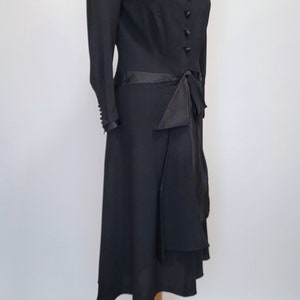 Puede incluir: Un vestido negro con una cinta de sat&eacute;n y un cuello negro contrastante. El vestido tiene un corpi&ntilde;o ajustado y una falda fluida.