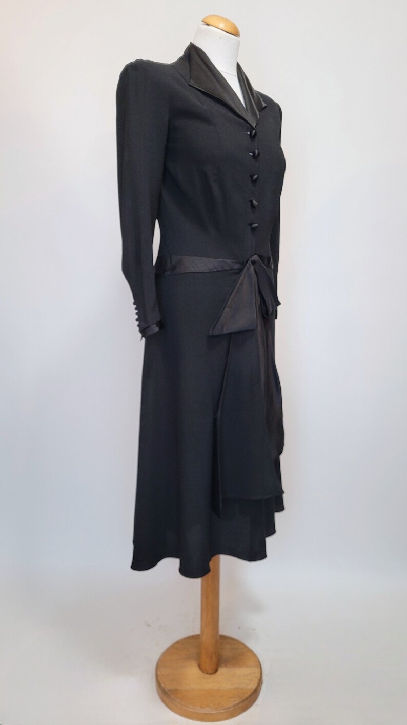 Puede incluir: Un vestido negro con una cinta de sat&eacute;n y un cuello negro contrastante. El vestido tiene un corpi&ntilde;o ajustado y una falda fluida.