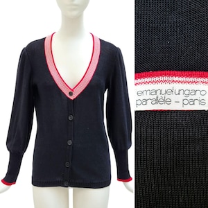 May include: Navy blue cardigan with a V-neck and button closure. The neckline and cuffs feature a red and white striped trim. The label reads "emanuel ungaro parallèle - paris".