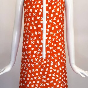 May include: A sleeveless orange dress with a white zipper and white geometric pattern. The dress has a white collar and two pockets.