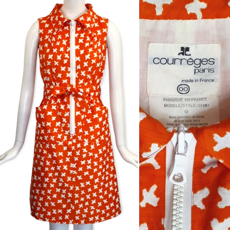 May include: Orange sleeveless dress with a white geometric pattern, a white zipper down the front, and a white belt. The dress has two pockets and a label that reads "courr&egrave;ges paris made in france 00 FABRIQUE EN FRANCE MODELE/STYLE:15301 0 WASH CAREFULLY IN WATER AT LESS THAN 150&deg;F RINCE WITH WARM WATER"